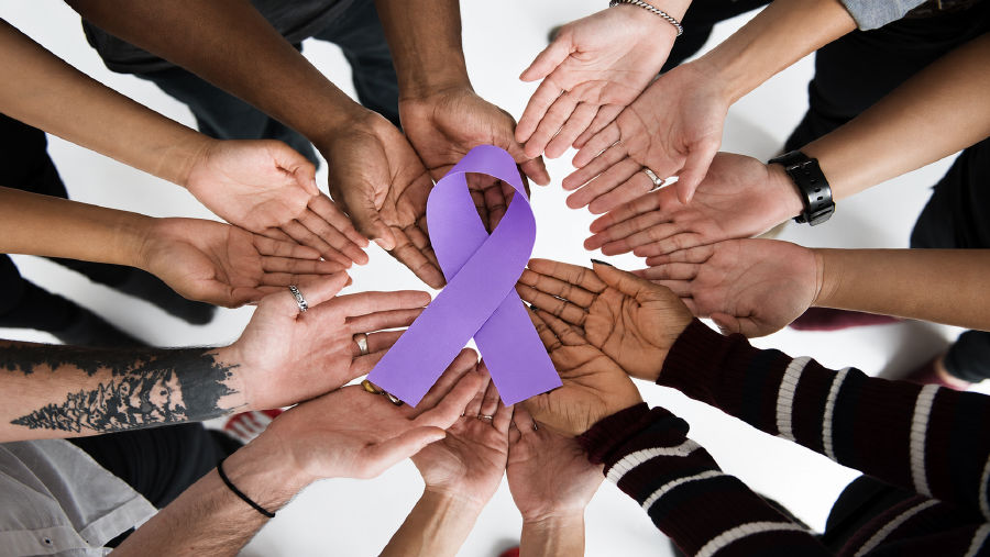 A diverse circle of hands joined together around a purple pancreatic cancer awareness ribbon, symbolizing community and support.
